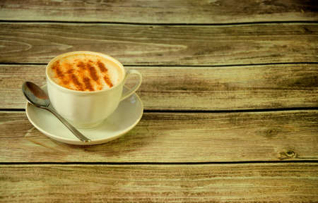 A porcelain cup of fresh cappuccino on a saucer decorated with cinnamon sticks and anise stands on a...