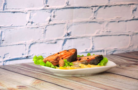 A plate with two slices of grilled pink salmon with a leaf of salad and slice of lemon. Close-up.