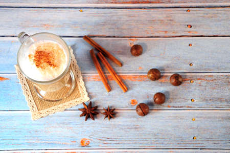 Glass latte mug on a napkin, next to cinnamon sticks, anise and macadamia nuts. Still life close-up.の写真素材