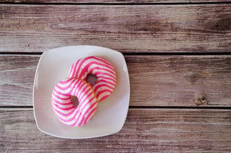 Two round donuts in pink glaze on a plate stand on a wooden table. Close-up.の写真素材