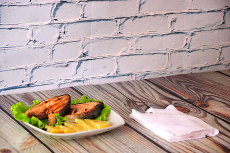 Two steaks of pink salmon fillet on a plate decorated with lettuce and slices of lemon are on a...