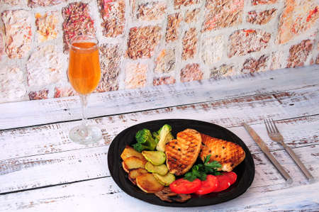A black plate with two steaks of grilled chicken with vegetables and a glass of wine stand on a...