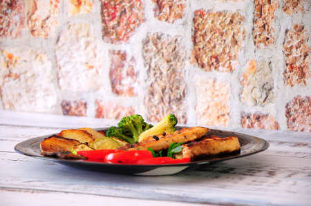 Two grilled steaks of chicken fillet, broccoli, tomato and potatoes on a large glass plate....