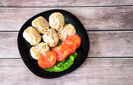Plate with freshly cooked manti on a lettuce sheet and sliced tomato on a wooden table. Flat lay.の写真素材