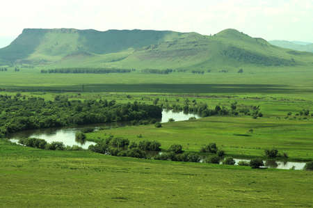 A picturesque valley with a winding river flowing through it and high mountains in the background....