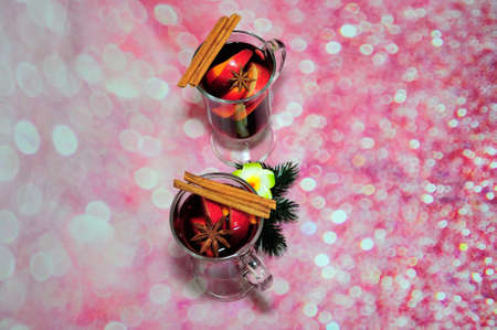 Two glasses of red hot wine with cinnamon and anise on a pink glittering background. Close-up.