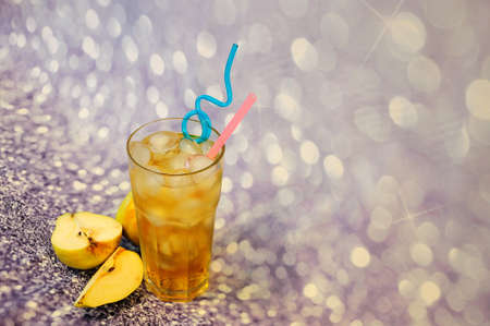 Tall glass of pear juice with ice and slices of ripe fruit nearby on a gray background. Close-up.