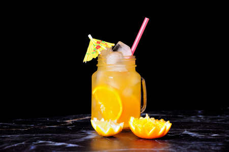 A glass mug with orange and lemon slices decorated with ice and an umbrella stands on a marble table. Close-up.の写真素材