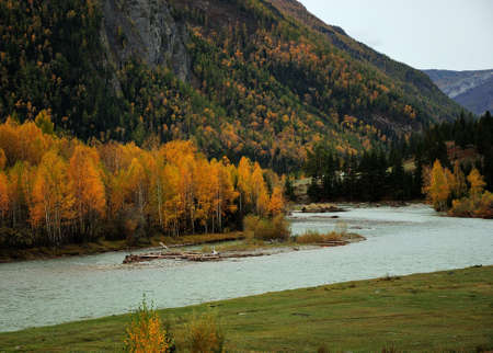 a beautiful winding turquoise river flows in autumn through a narrow valley surrounded by mountains....