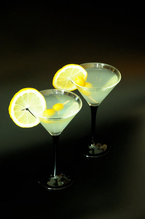 Two glasses of white vermouth with olives and lemon slices on a black background. Close-up.の写真素材