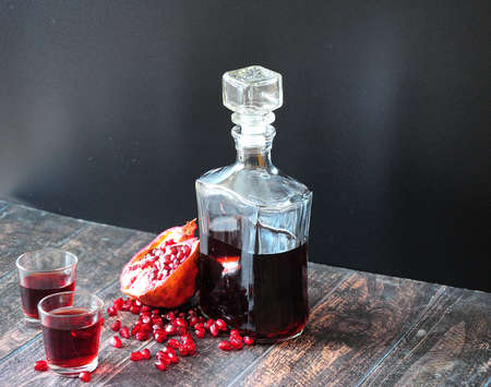 Pomegranate liqueur in a glass decanter and two glasses stands on a wooden table against a black...