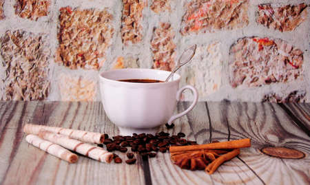 A cup of black coffee on a wooden table with cinnamon, anise and waffle rolls. Close-up.の写真素材