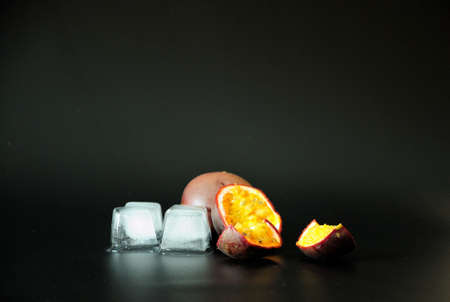 Ripe exotic passionfruit cut into slices and melted ice cubes on a black background. Close-up.