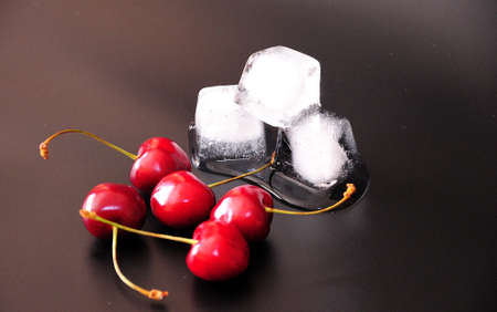 A handful of ripe cherries with twigs and cubes of melted ice on a black background. Close-up.の写真素材
