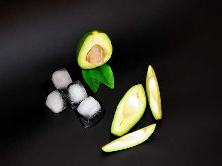 Cut ripe avocado and melted ice cubes on a black background. Close-up.の写真素材