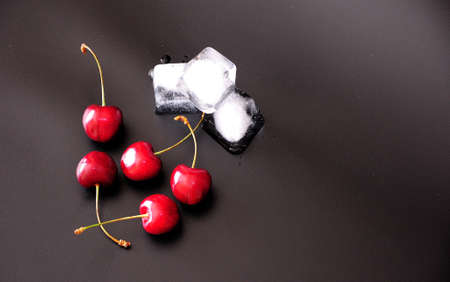 A pile of ripe cherries and cubes of melted ice on a black background. Close-up.の写真素材