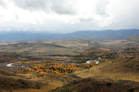 A view of a beautiful winding river flowing through a wide valley along a mountain range with...