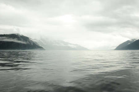 A look at the picturesque mountain lake and clouds descending to the water from the tops of the hills in cloudy weather. Teletskoye lake, Altai, Siberia, Russia.の写真素材