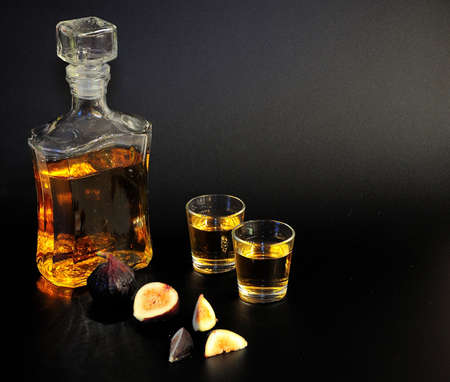 Homemade fig liqueur, glass decanter and two glasses of drink and ripe fruit pieces on a black background. Close-up.の写真素材