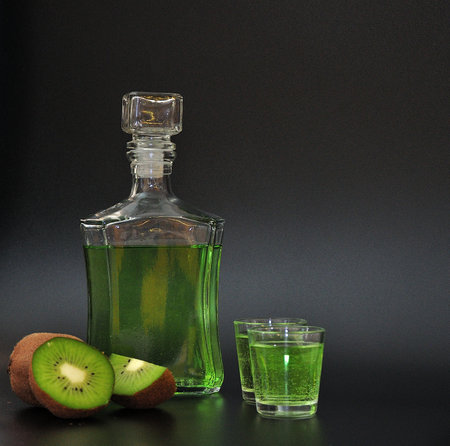Homemade kiwi-based liqueur in two glasses and a glass bottle, ripe fruits next to it on a black background. Close-up.の写真素材