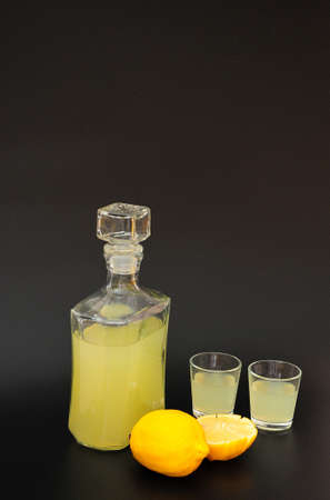 Lemon liqueur, strong alcohol in glasses and a glass decanter on a black background, next to pieces of ripe citrus. Close-up.の写真素材