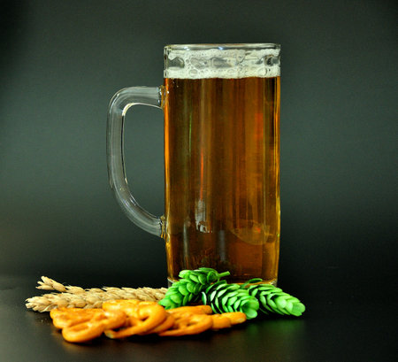 A glass mug with a handle full of light beer on a black background, barley ears and hops next to it. Close-up.の写真素材