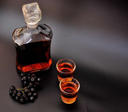 Blackcurrant liqueur, strong homemade alcohol in a bottle and two glasses on a black background. Close-up.の写真素材