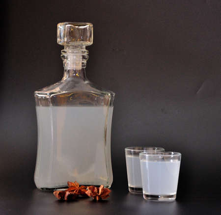 Anise liqueur, strong homemade alcohol, a bottle and two glasses with a drink on a black background,...