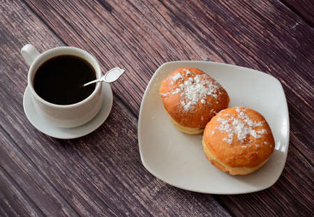 A cup of fresh black coffee and a plate with two donuts in powdered sugar on a wooden table. Top view, flat lay.の写真素材