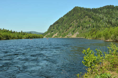 A wide river turns into a swift stream at the foot of a high mountain. Biya river, Altai, Siberia,...