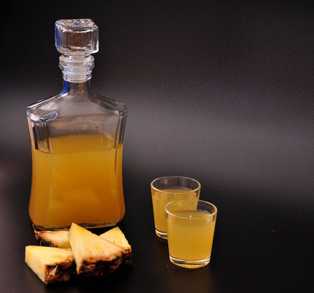 Pineapple liqueur, light homemade alcohol and pieces of ripe fruit on a black background. close-up.の写真素材