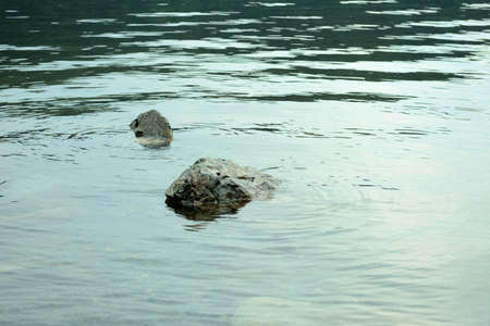 Two stones sticking out from under the surface of the water of a large lake leave undulating ripples...