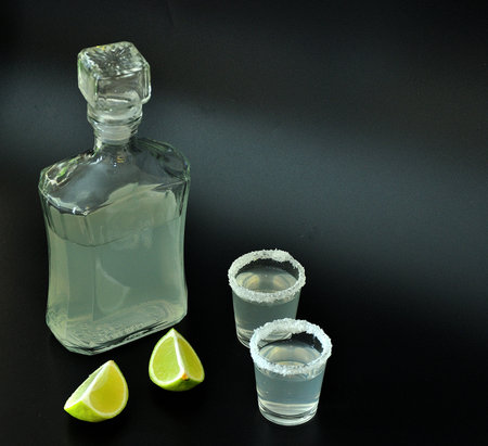 A bottle of tequila and two glasses on a black background, next to pieces of salt and lime. close-up.の写真素材