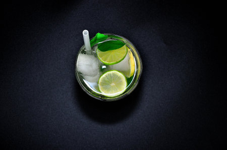 A glass of lime juice with citrus pieces, ice and a straw on a black background. Top view, flat lay.の写真素材