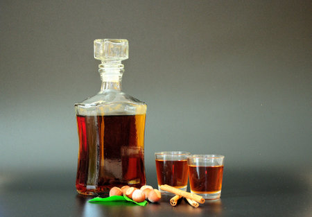 Nut liqueur with cinnamon and mint leaves, a bottle and two glasses with strong alcohol on a black background. close-up.の写真素材
