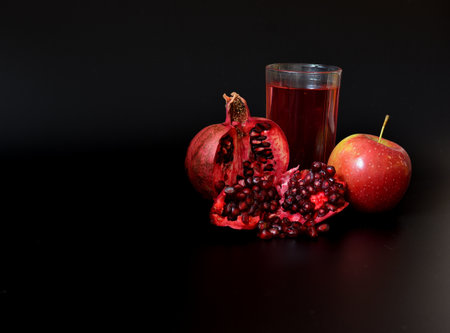 Ripe broken pomegranate and red apple near a glass of fresh fruit juice on a black background. close-up.の写真素材