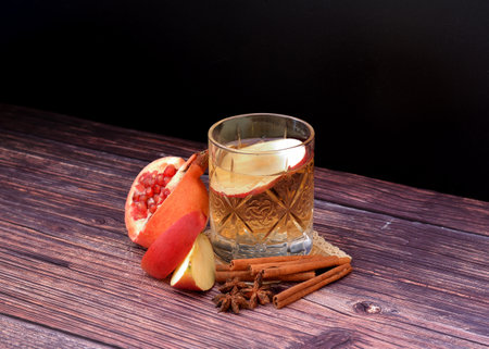 A crystal glass of apple cider with pomegranate, cinnamon and anise on a wooden table, next to pieces of fruit. close-up.の写真素材