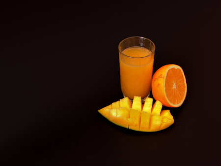 A glass of a mixture of juices from tropical fruits on a black background, next to a half of an...