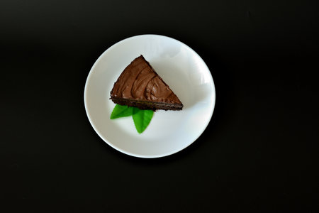 Round and white ceramic plate with a piece of chocolate cheesecake decorated with mint leaves on a black background. Top view, flat lay.の写真素材