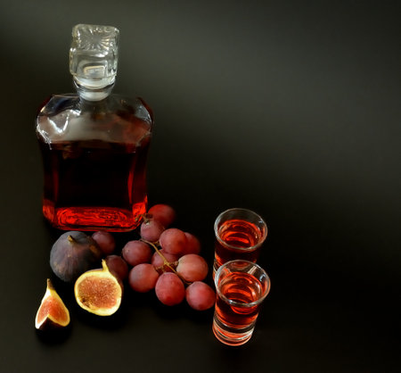 Grape-fig liqueur on a black background, a bottle and two glasses of alcohol, ripe fruits nearby. close-up.の写真素材