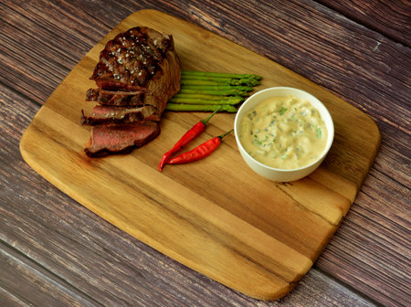 Wooden plate with fried beef steak with asparagus and hot peppers on a wooden table, sauce and cutlery nearby. Top view, flat lay.の写真素材