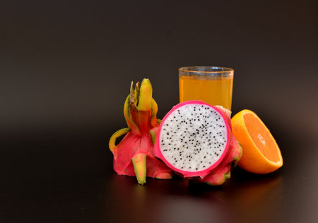 A glass of fruit juice on a black background, next to pieces of ripe orange and pitaya. close-up.の写真素材