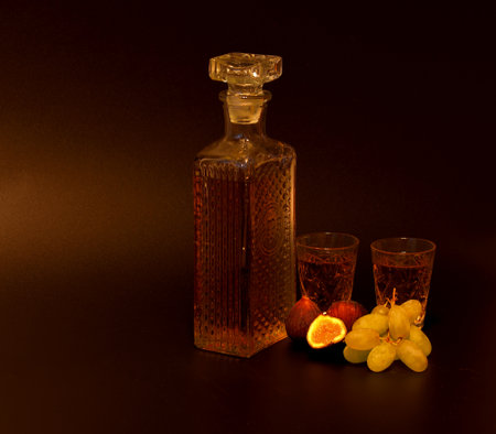 Grape-fig liqueur on a black background, a bottle and two crystal glasses with strong homemade alcohol, next to ripe fruits. Close-up.の写真素材