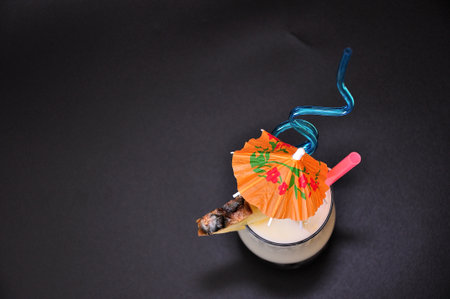 A tall glass with a refreshing Pina Colada cocktail with ice, straws and a piece of pineapple on a black background. Top view, flat lay.の写真素材