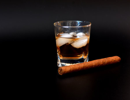 Cuban cigar and glass of whiskey with ice on a black background. Close-up.の写真素材