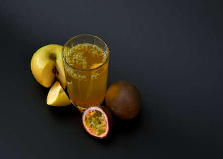 A tall glass of fruit juice with seeds on a black background, next to a ripe passion fruit and...