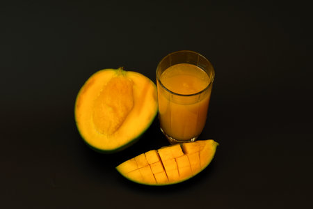 A tall glass of freshly squeezed tropical fruit juice and ripe mango slices on a black background. Close-up.の写真素材