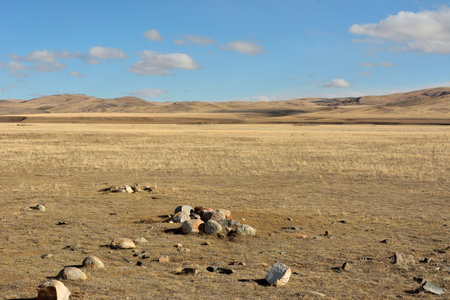 Remains of an ancient stone sanctuary in a wide flat steppe at the foot of high snow-capped mountains on a sunny autumn day.の写真素材