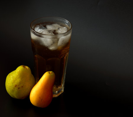 Fruit juice in a tall faceted glass with ice on a black background, next to ripe yellow and green pear fruits. Close-up.の写真素材