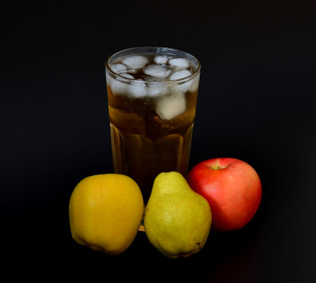 A tall glass of a mixture of fruit juices with ice on a black background, next to ripe apples and pears. Close-up.の写真素材